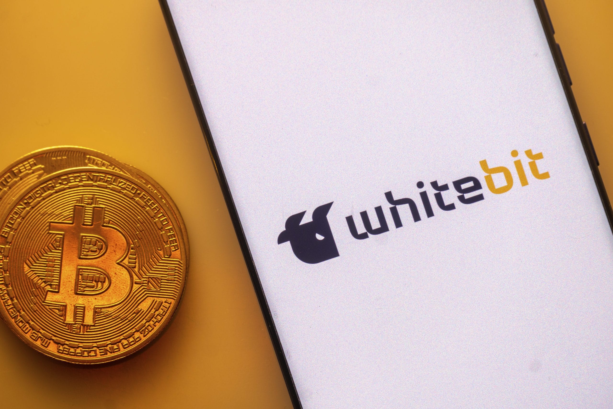 Das Bild zeigt das WhiteBIT-Logo und eine Bitcoin-Münze