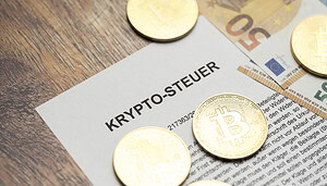 Ein paar Bitcoin-Münzen liegen auf einem Blatt auf dem Krypto-Steuer steht.