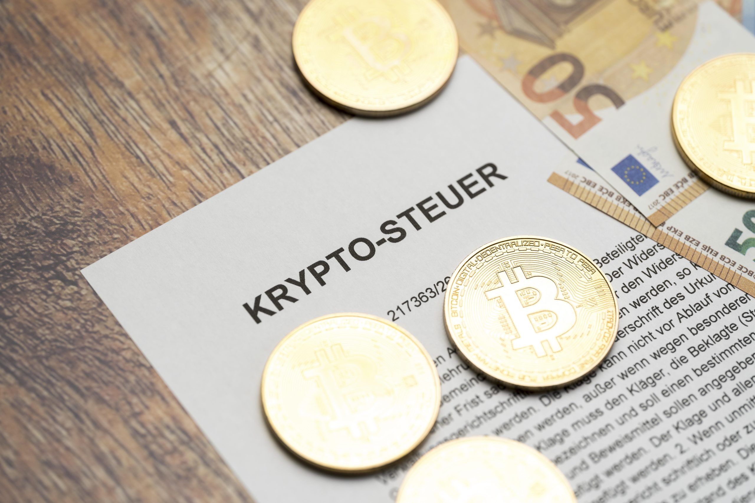 Ein paar Bitcoin-Münzen liegen auf einem Blatt auf dem Krypto-Steuer steht.