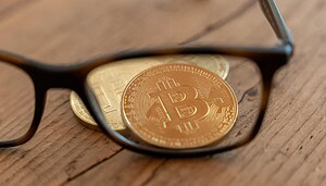 Das Bild zeigt eine Brille und eine Bitcoin-Münze