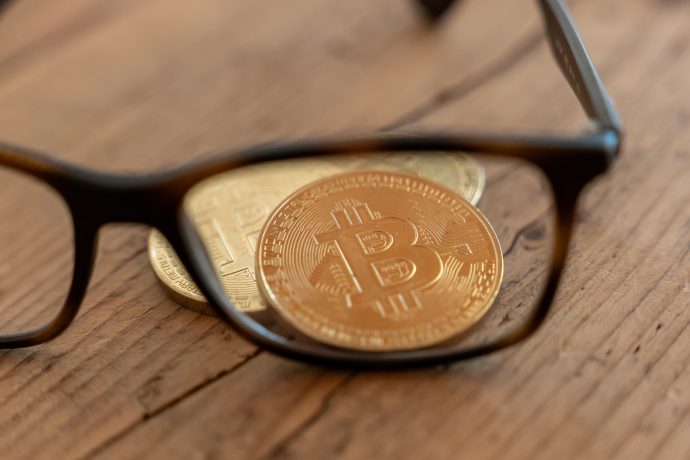 Das Bild zeigt eine Brille und eine Bitcoin-Münze