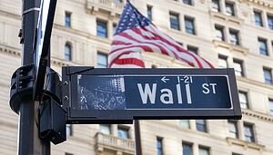 Das Straßenschild der Wall Street vor einer US-Flagge.