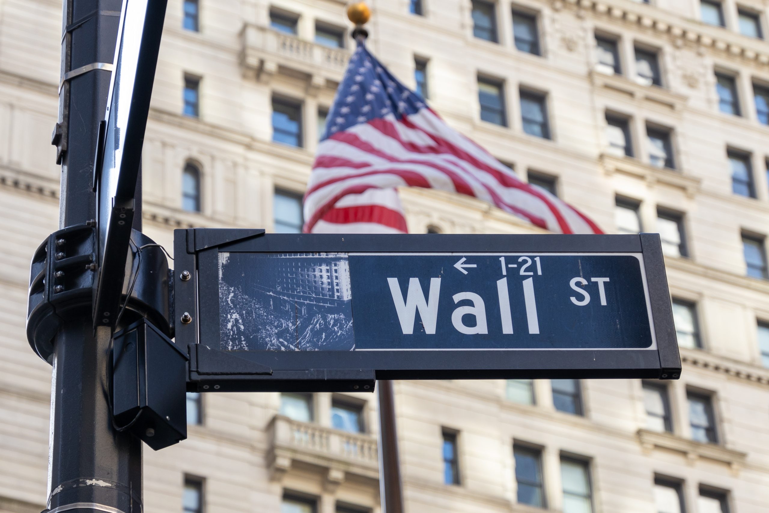 Das Straßenschild der Wall Street vor einer US-Flagge.