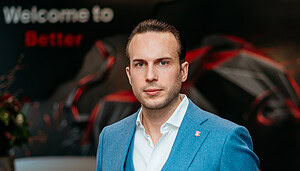 Ein Mann mit blauem Anzug steht vor einem Hintergrund in den Farben der Bitcoin Suisse