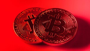 Das Bild zeigt zwei Bitcoin-Münzen auf rotem Hintergrund.