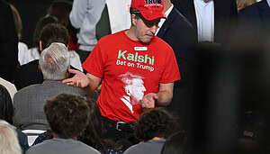 Ein Mann trägt eine rote Mütze mit der Aufschrift Trump und eine rotes T-Shirt mit der grünen Aufschrift Kalshi.