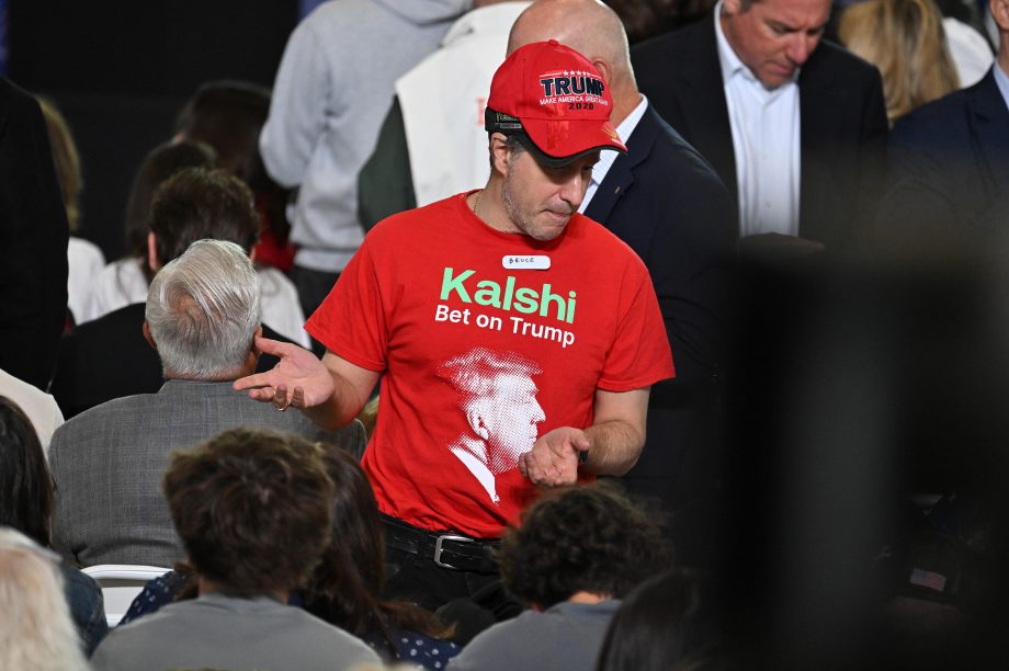 Ein Mann trägt eine rote Mütze mit der Aufschrift Trump und eine rotes T-Shirt mit der grünen Aufschrift Kalshi.