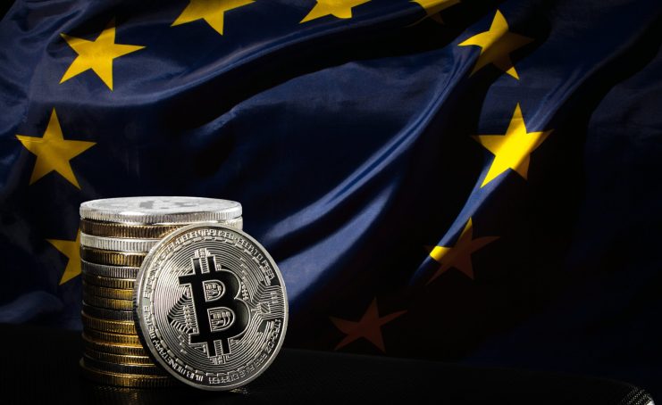 Was passiert unter der MiCAR? Gestapelte silberne Bitcoin-Münzen befinden sich vor einer Flagge der Europäischen Union mit sichtbaren gelben Sternen auf dunkelblauem Hintergrund.