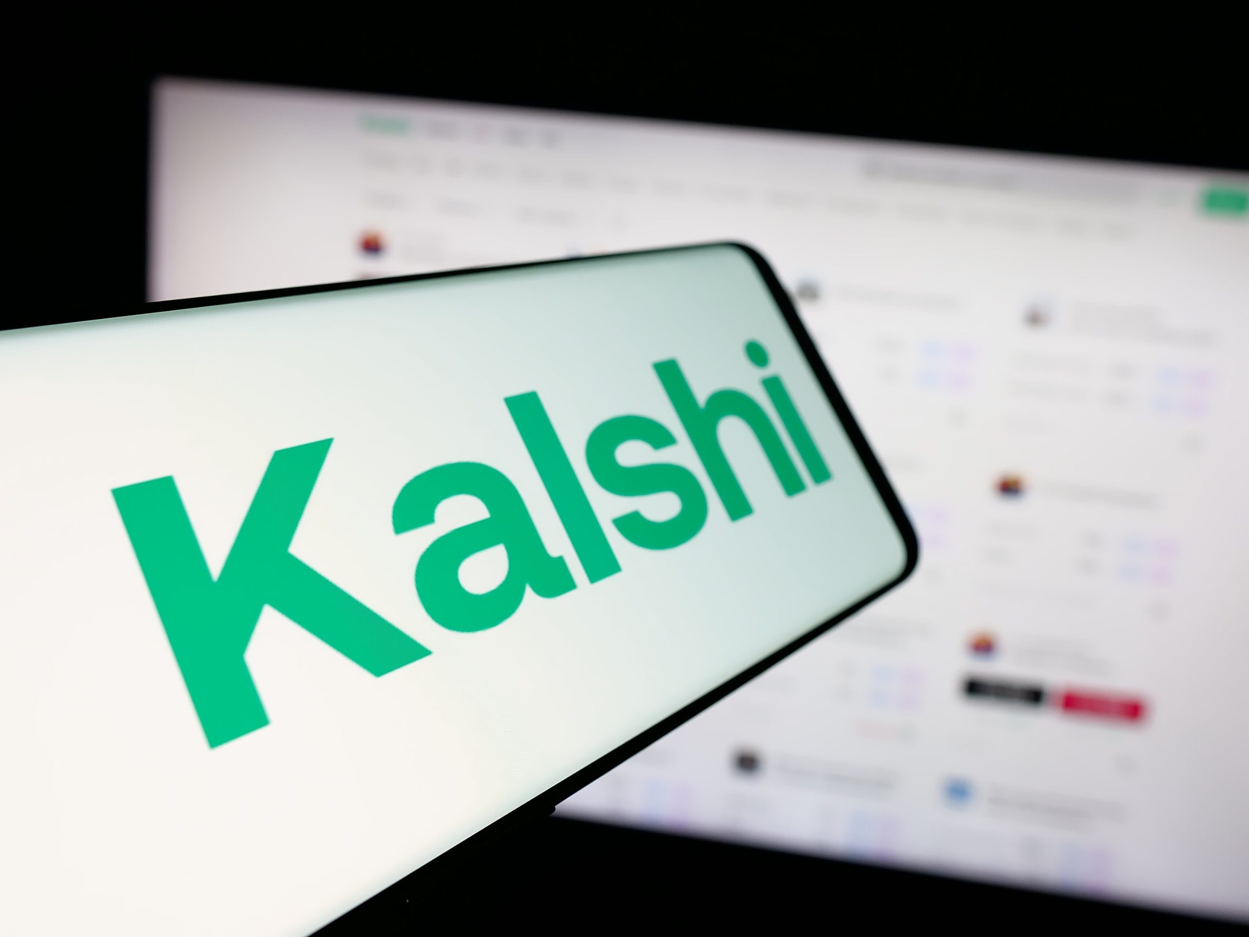 Kalshi-Logo auf einem Smartphone vor einem Computerbildschirm.