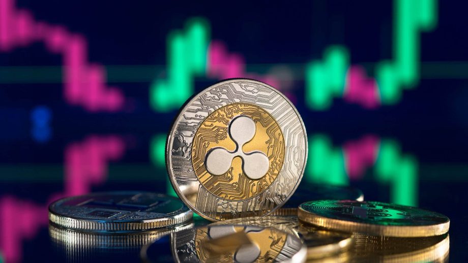 Eine Nahaufnahme von Ripple (XRP)-Kryptowährungsmünzen auf einer spiegelnden Oberfläche mit einem digitalen Preisdiagramm, das den XRP-Kurs und leuchtend grüne und rosafarbene Kerzenleuchter im Hintergrund zeigt.