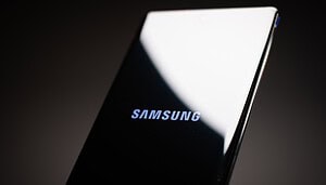Nahaufnahme eines Samsung-Smartphones, auf dessen Bildschirm das Samsung- und das Coinbase-Logo vor einem dunklen Hintergrund zu sehen sind.