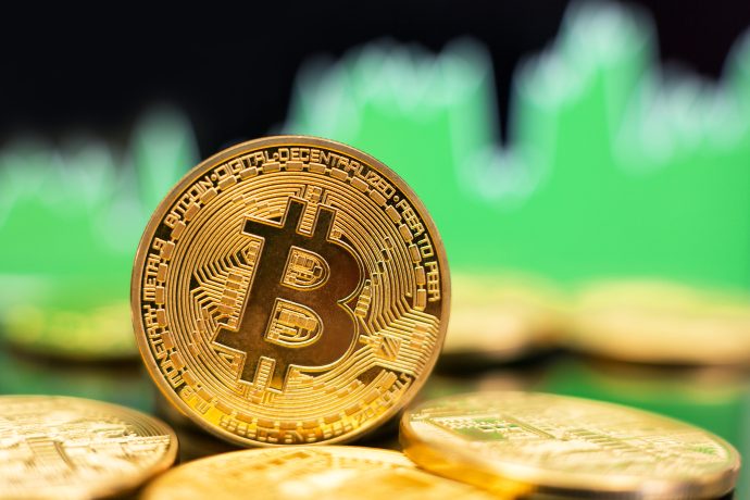 Eine goldene Bitcoin vor einem grünen Charthintergrund.