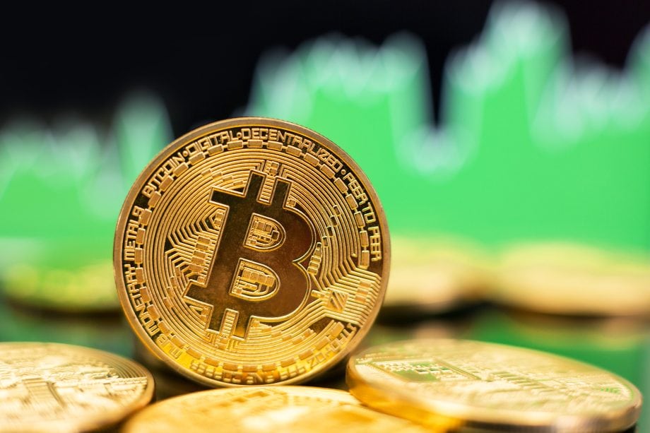 Eine goldene Bitcoin vor einem grünen Charthintergrund.