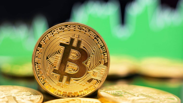 Eine goldene Bitcoin vor einem grünen Charthintergrund.