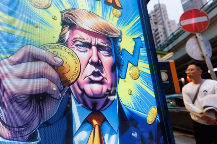Das Bild zeigt ein großformatiges Werbedisplay im öffentlichen Raum mit einer stilisierten Darstellung von Donald Trump, der eine Bitcoin-Münze in die Kamera hält.