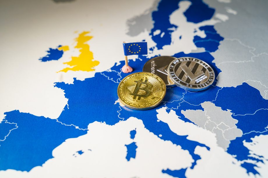 Man sieht die Karte Europas mit Hervorhebung der EU-Länder. Auf der Karte liegt eine Bitcoin-Münze und zwei andere Krypto-Coin-Münzen ab.