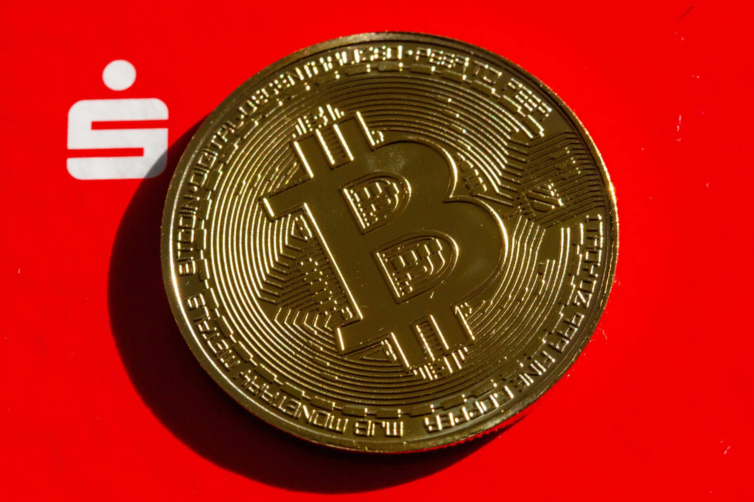 Das Bild zeigt eine Bitcoin-Münze vor dem Logo der Sparkassen