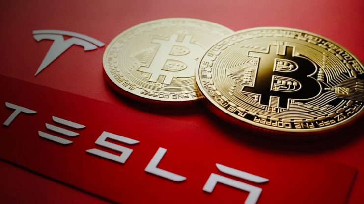 Das Bild zeigt das Tesla-Logo und Bitcoin-Münzen
