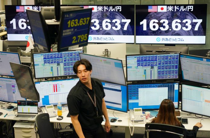 Das Bild zeigt eine Kurstafel in einem Tokioter Handelsraum mit einem Dollar-Yen-Kurs von 163,637.