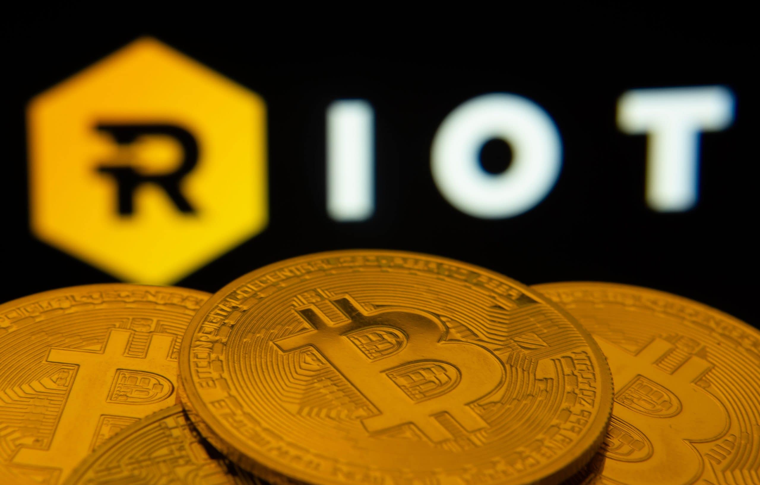 Das Bild zeigt den Namen des Bitcoin Miners Riot und einige Bitcoin-Münzen.