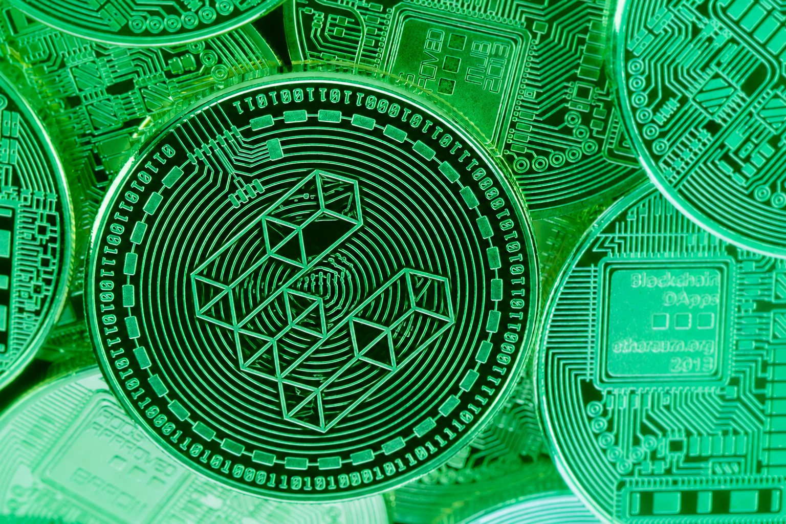 Nahaufnahme einer grün beleuchteten Ether.fi-Münze mit eingeprägtem geometrischem Logo, umgeben von weiteren digitalen Münzen mit Leiterplattenmustern.