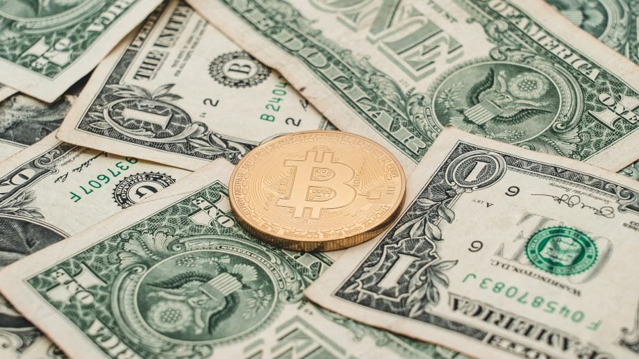 Das Bild zeigt eine Bitcoin-Münze auf US-Dollar-Scheinen