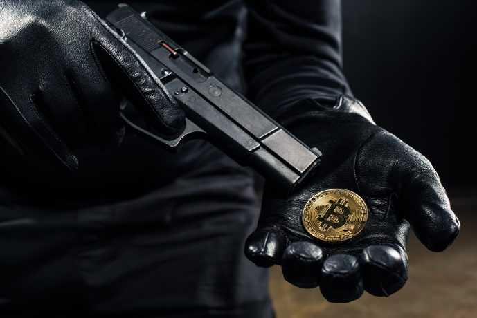 Eine Hand richtet eine Pistole auf eine Bitcoin-Münze