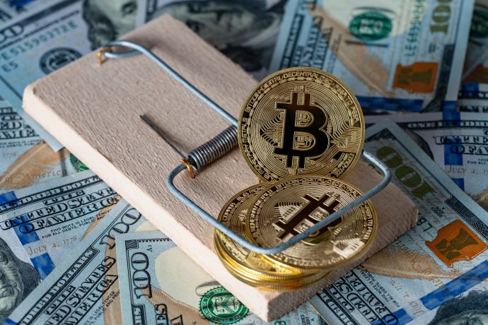 Bitcoin-Münzen in einer Mausefalle, dahinter Dollarscheine