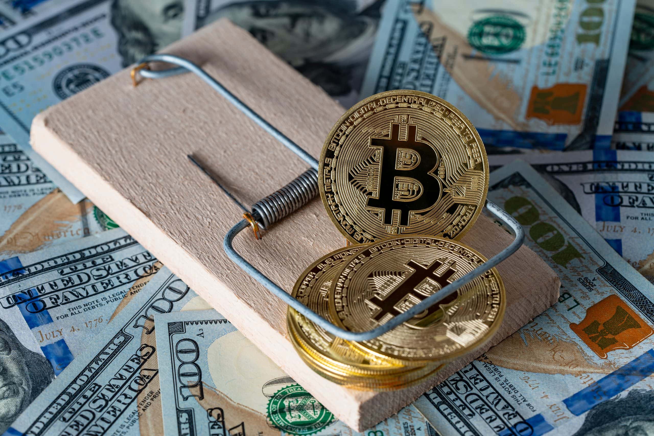 Bitcoin-Münzen in einer Mausefalle, dahinter Dollarscheine