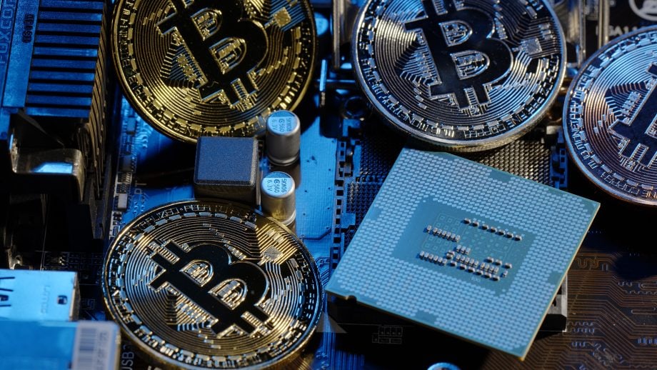 Mehrere Bitcoin-Münzen und ein Prozessor liegen auf einer blau beleuchteten Hauptplatine.