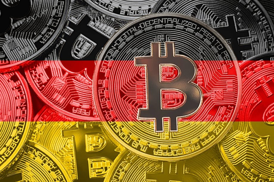 Man sieht mehrere Bitcoin-Münzen vor dem Hintergrund der Farben der Deutschland-Flagge