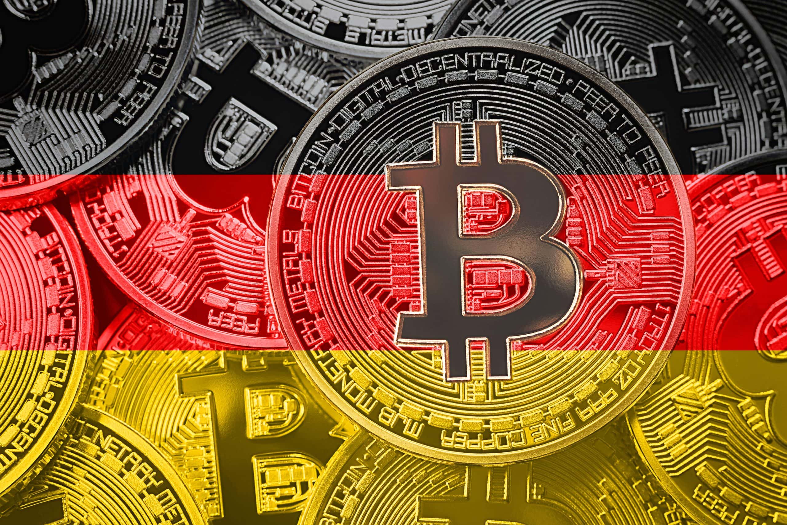 Man sieht mehrere Bitcoin-Münzen vor dem Hintergrund der Farben der Deutschland-Flagge