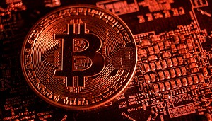 Eine Bitcoin-Münze liegt rot ausgeleuchtet auf einem Computerchip