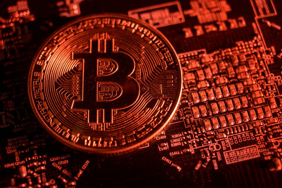 Eine Bitcoin-Münze liegt rot ausgeleuchtet auf einem Computerchip