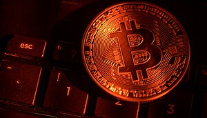 Eine rot beleuchtete Bitcoin-Münze liegt auf einer Tastatur
