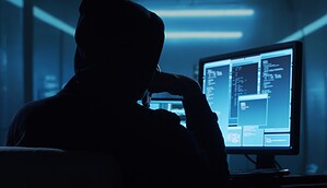 Das Bild zeigt einen Hacker vor einem Bildschirm