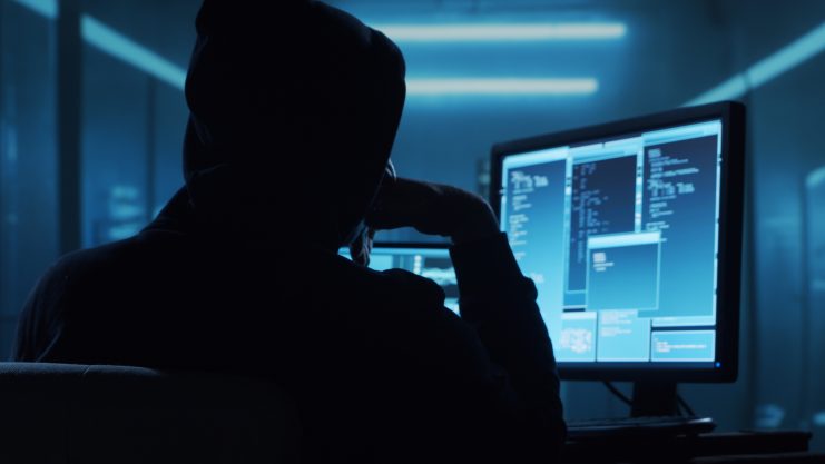 Das Bild zeigt einen Hacker vor einem Bildschirm