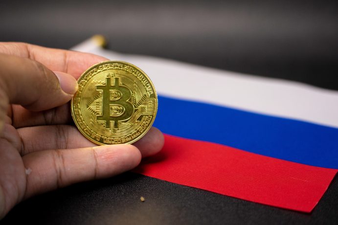 Das Bild zeigt eine Bitcoin-Münze und die russische Flagge