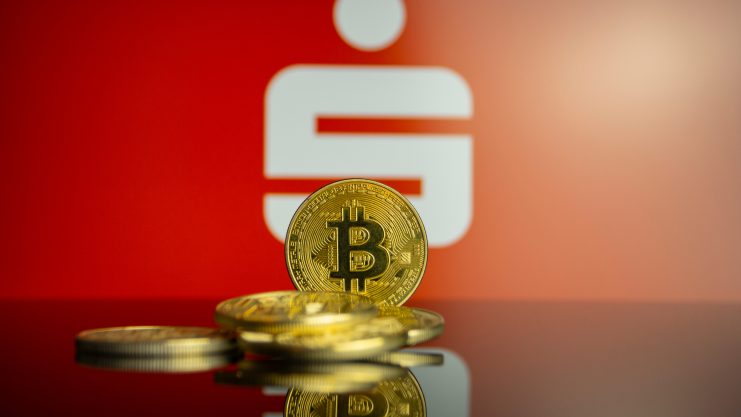 Eine Bitcoin-Münze vor dem Sparkassen-Logo