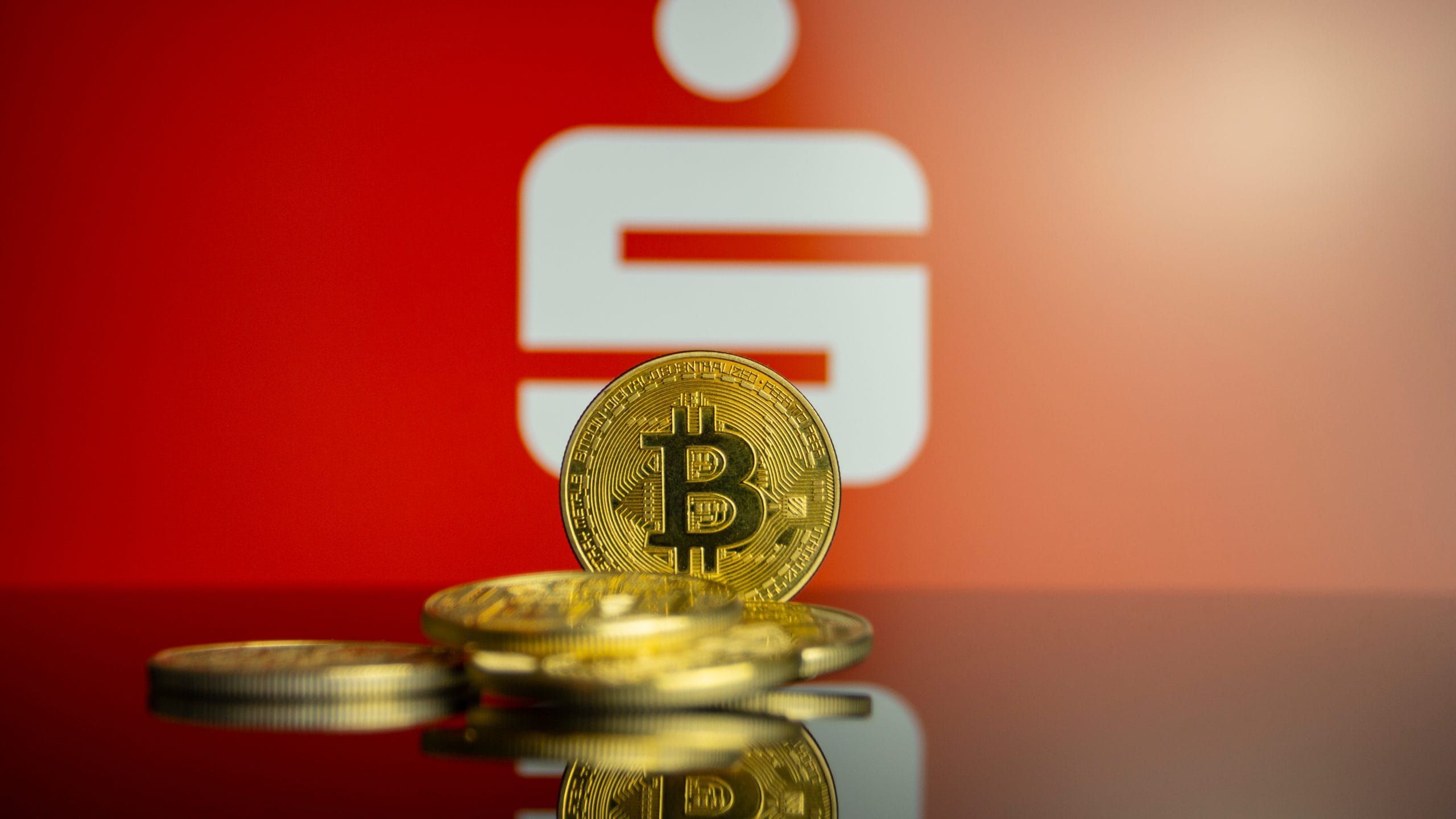 Eine Bitcoin-Münze vor dem Sparkassen-Logo