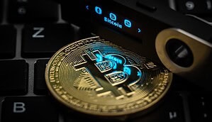 Der Schriftzug Bitcoin ist auf dem Display eines Ledger Nano S Hardware Wallets neben einer symbolischen „Bitcoin Münze“ zu sehen.