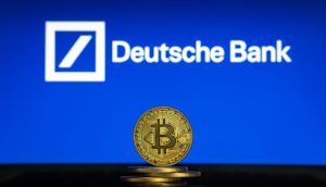 Ein Stapel physischer Bitcoin-Token wird vor einem Bildschirm gezeigt, auf dem das Logo der Deutschen Bank auf blauem Hintergrund zu sehen ist.