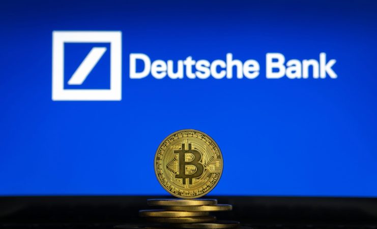 Ein Stapel physischer Bitcoin-Token wird vor einem Bildschirm gezeigt, auf dem das Logo der Deutschen Bank auf blauem Hintergrund zu sehen ist.