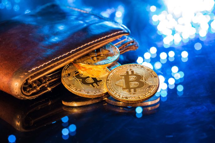 Eine Bitcoin Wallet liegt auf dem Tisch und die Münzen fallen heraus.