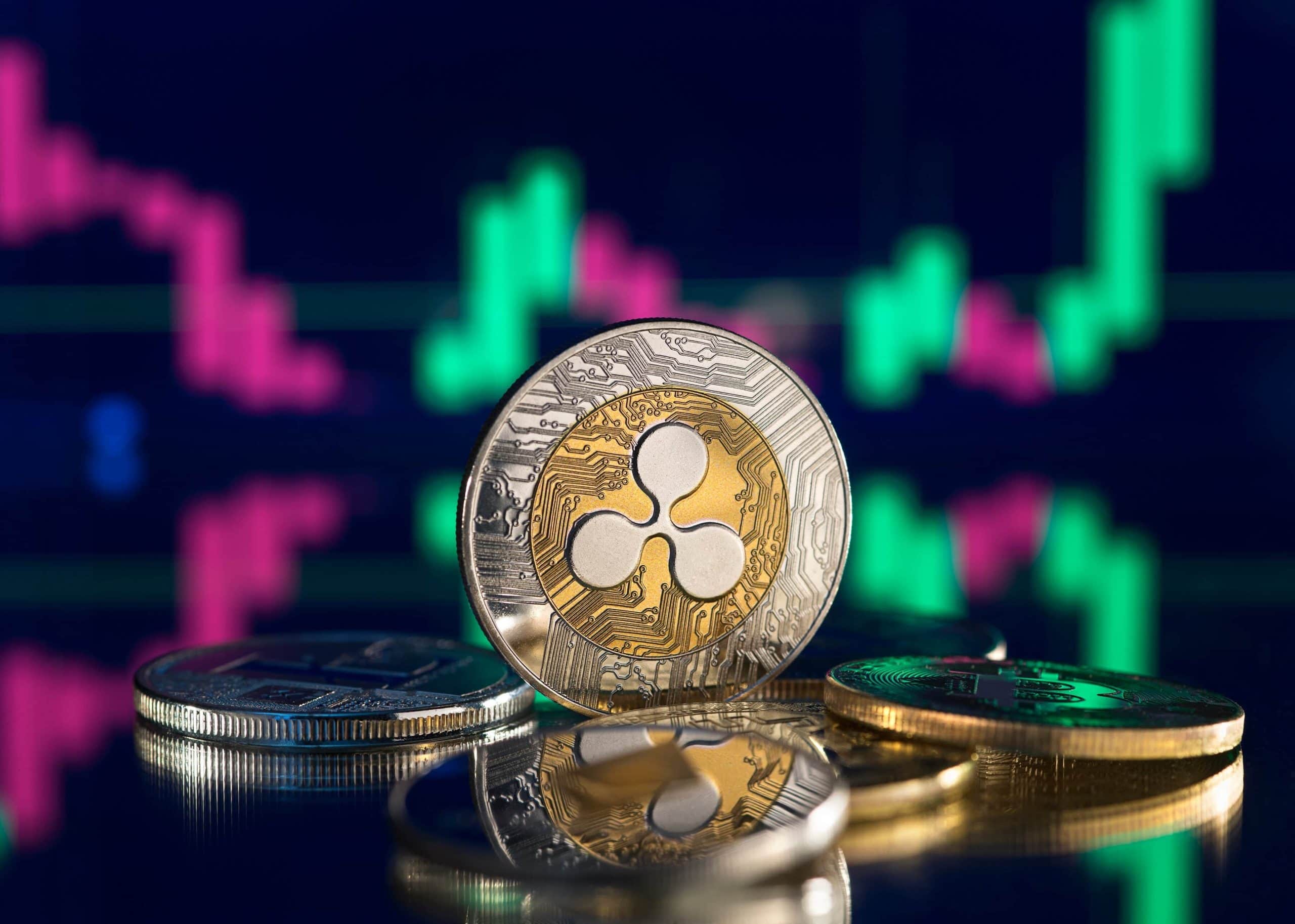 Eine Nahaufnahme von Ripple (XRP)-Kryptowährungsmünzen auf einer spiegelnden Oberfläche mit einem digitalen Preisdiagramm, das den XRP-Kurs und leuchtend grüne und rosafarbene Kerzen im Hintergrund zeigt.