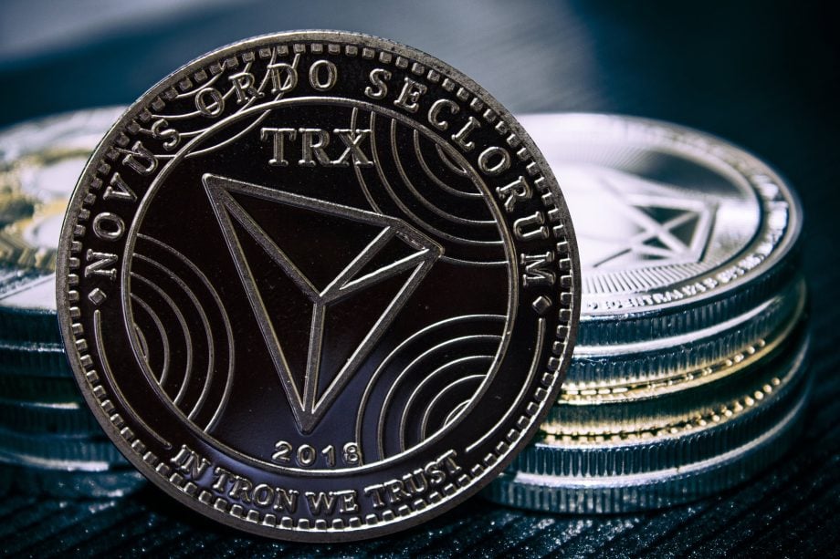 Eine Nahaufnahme einer Tron (TRX) Kryptowährungsmünze steht aufrecht vor gestapelten Münzen