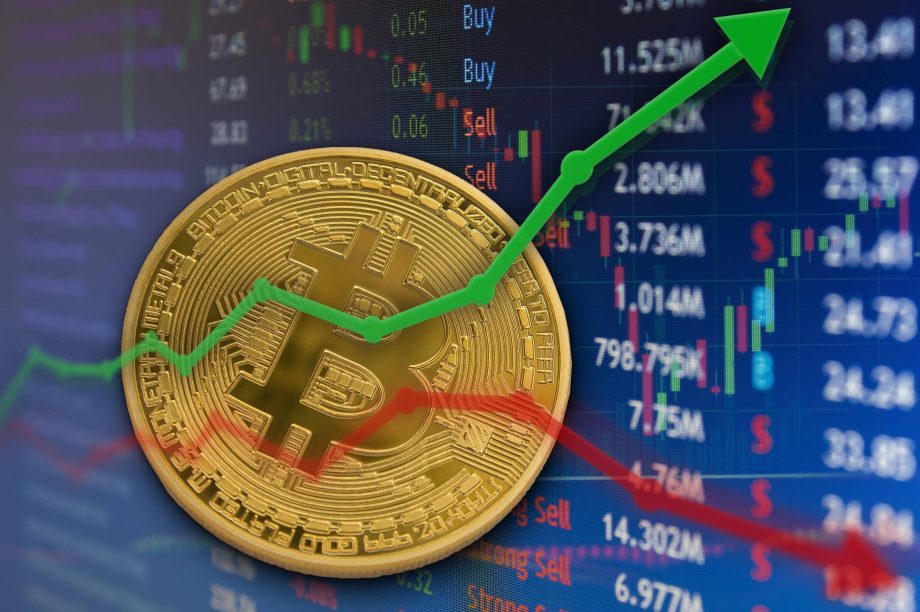 Man sieht eine Bitcoin-Münze und einen grünen Pfeil nach oben sowie einen roten Pfeil nach unten. Im Hintergrund sieht man Kursdaten.