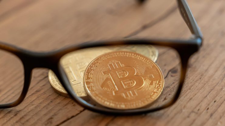 Das Bild zeigt einen Bitcoin-Münze und eine Brille