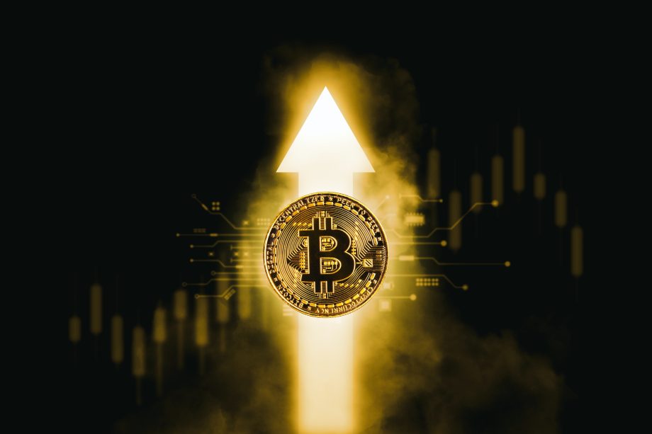 Bitcoin-Bärenmarkt: Goldene Bitcoin-Münze vor einem leuchtenden Pfeil nach oben und Kerzen eines Kurscharts auf schwarzem Hintergrund