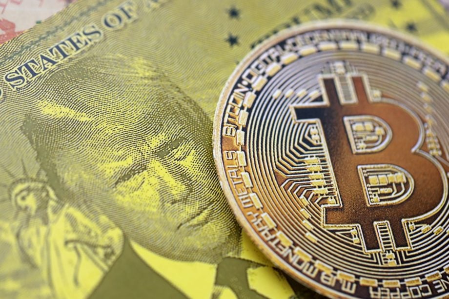 Eine Bitcoin-Münze auf einem fiktiven Geldschein, der DOnald Trump zeigt